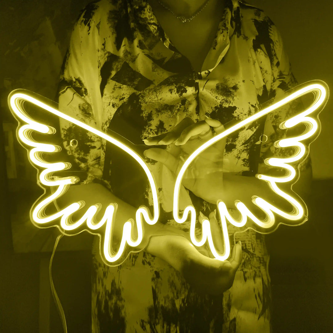 A girl holding a custom neon sign of yellow color in the shape of angel wings | ManhattanNeons