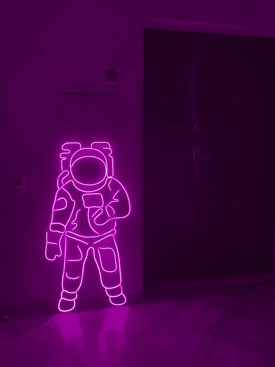 Purple colored Astronaut LED Neon Sign placed on the floor beside a door - from manhattonneons.com.